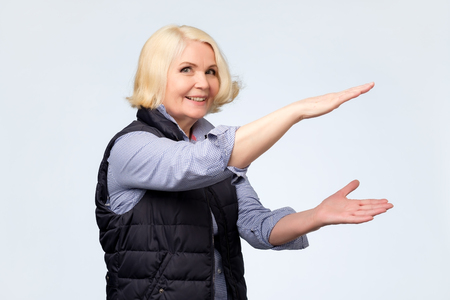 Happy smiling senior woman making showing big size thing. Positive facial emotion.の写真素材