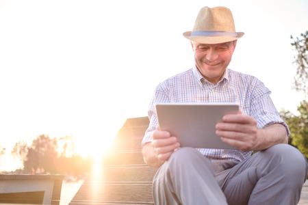 Hispanic senior man in summer hat reading tablet in park copy spaceの写真素材