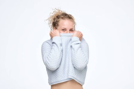Curly blonde girl pulling sweater over head having fun being shy and childishの写真素材