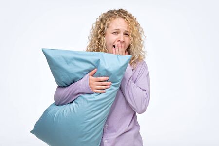Pretty curly tired girl yawning holding blue pillow.の写真素材