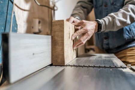Man making wooden parts for furniture on thickness planer machine.