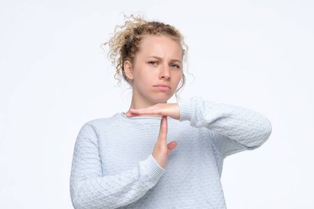 Blonde curly woman in blue sweater making time out gesture