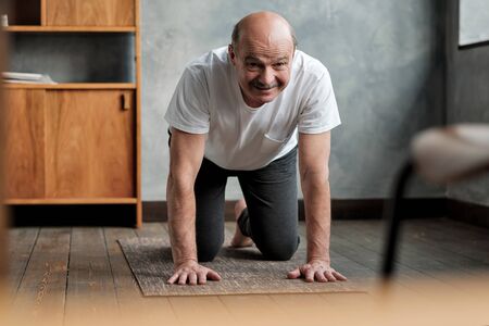 Senior hispanic man practices yoga asana marjariasana or cat-cow pose at home.の写真素材