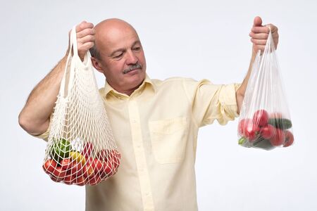 String bag versus plastic one. Mature hispanic man choosing a cotton bag for his shopping.の写真素材