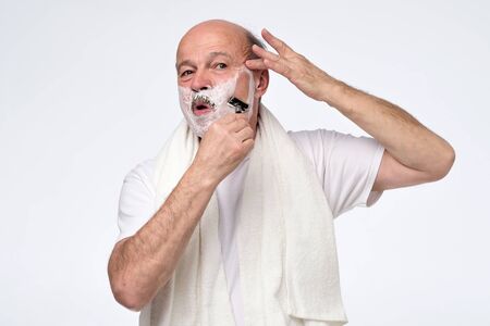 Senior man shaving skin in the morning. Using white foam and sharp razor or blade. Studio shotの写真素材