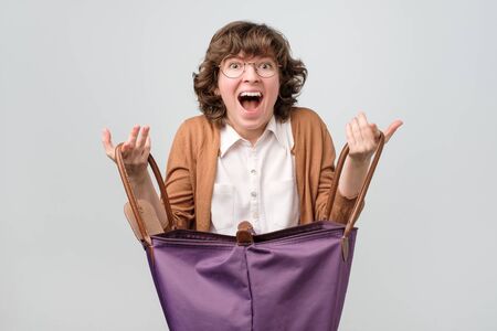 Young funny woman with big shopping bag being happy to find something inside