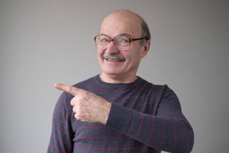 Confident hispanic senior man point aside. Serious mature male gesturing with his finger aside