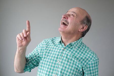 Bald mature hispanic man looking up pointing up laughing.の写真素材