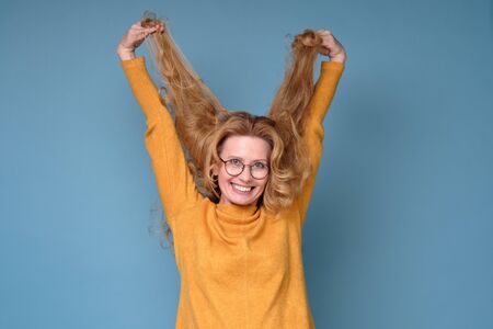Mature woman looking at the camera, playing with her long blonde hair.