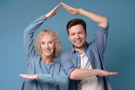 Mature mother and son holding hands like house gesture.