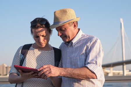 Senior man in summer hat and young girl searching for right way using tablet.の写真素材