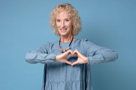Love, heart shape, peace. Cute attractive smiling blonde woman shows heart sign with help of her...