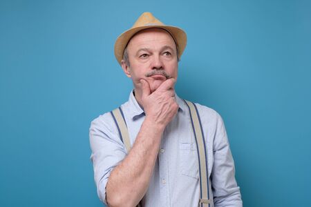 Senior man in summer hat thinking and rubbing chin trying to make a solution.の写真素材