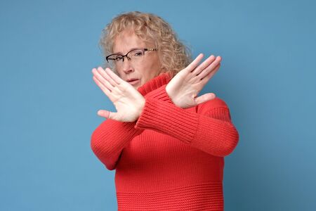 Middle age mature woman wearing red sweater and glasses doing stop gesture