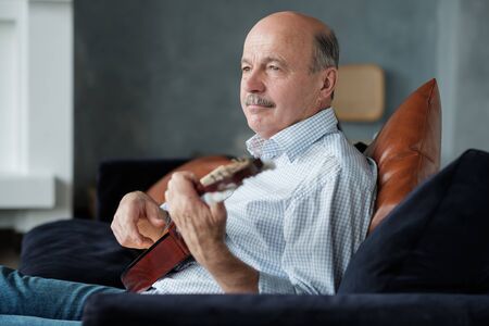 Senior man playing acoustic guitar at homeの写真素材