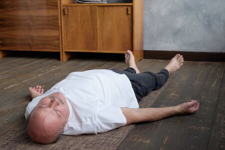 Yoga. Senior man meditating on a wooden floor and lying in Shavasana pose.の写真素材