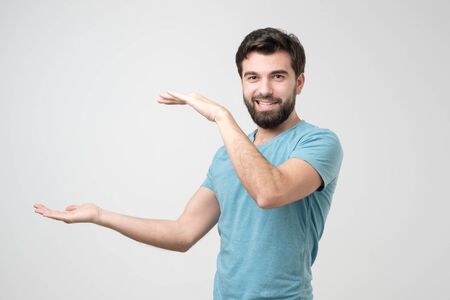 Hispanic young man with beard holding two hands in front of him and shows the size on white isolated background in studio.の写真素材