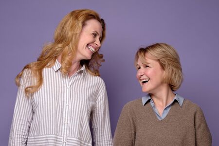 Two happy mature women sisters laughing and smiling looking at camera. Studio shot