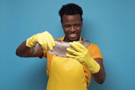 man in yellow t-shirt, gloves and apron looking with pleased expression at fish.の写真素材