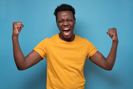 Amazed African American man in yellow clothes holding fists in surprised gestureの写真素材