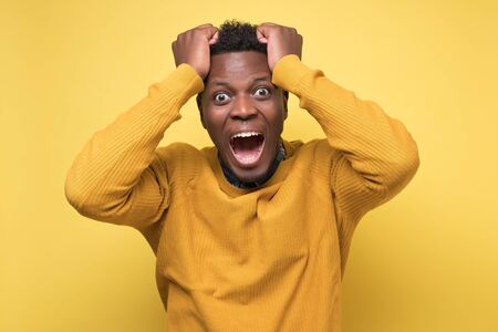 African male screaming in surprise, mouth wide open, holding hand on head