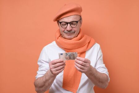 Senior man holding euro bank note stressed being confused and frustrated. It is his last money....