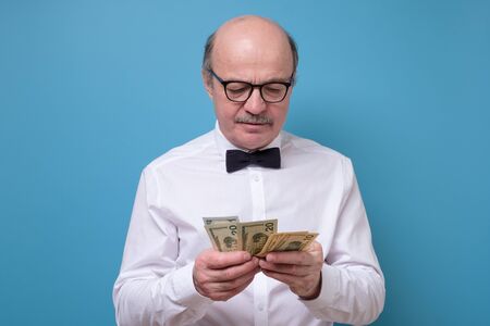 Hispanic male pensioner counting money dollars isolated on blue background