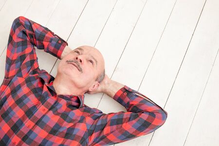 Lost in thoughts. Dreaming mature hispanic man lie on white floor looking away thinking about future...