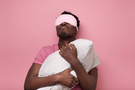 Sleepy dark haired man in mask holding white pillowの写真素材