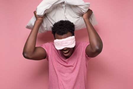 Young african man with pillow on head feeling good and amazed on pink wall.の写真素材