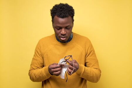 Young african american man cleaning glasses with a piece of tissueの写真素材