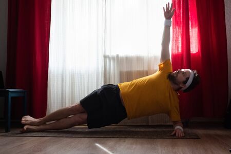 Cheerful man doing a side plank exercise at the roomの写真素材