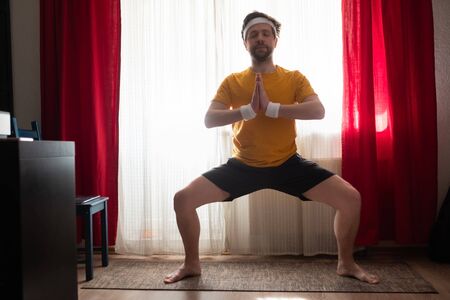 Young man working out, yoga, pilates, fitness training, Goddess Pose, temple or sumo pose, stupasana, rudrasana, exercise for knees, legs musclesの写真素材