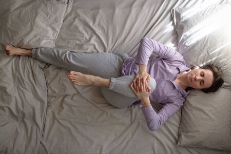 Sporty young woman lying on bed in the morning and doing stretching exercise from yoga pavanamuktasana. Top viewの写真素材