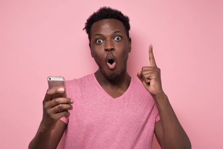 African american man received an sms from his bank with shocked face. Studio shot on pink wall.の写真素材