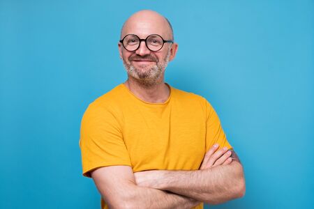 Portrait of smiling man in yellow clothes and glasses. Studio shot on blue wall.の写真素材