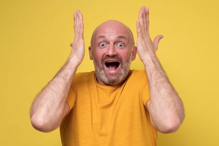 Amazed mature man holding hands in surprised gesture, keeping mouth wide openの写真素材