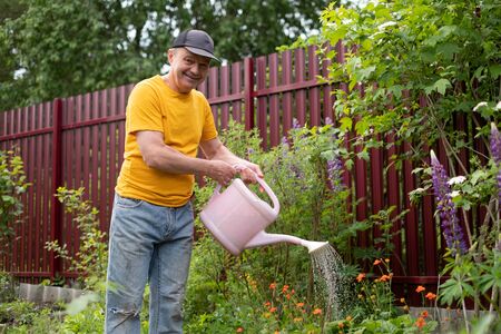 man watering flowers using can in his garden.