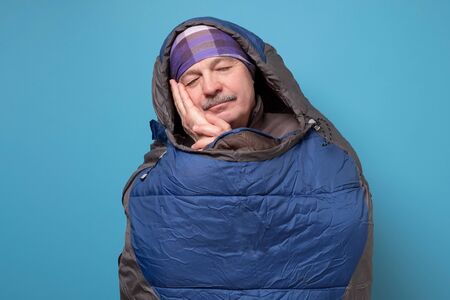 Senior man in comfortable sleeping bag on blue wall.の写真素材