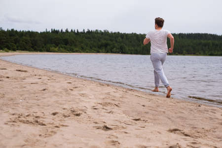Young caucasian man in fitness clothing running along sandy beach. Rear viewの写真素材