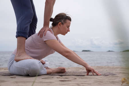 Man helping woman to do a yoga exercise butterfly pose or Baddha Konasana
