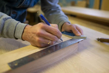 View of a carpenter using a pencil to draw a line on a wooden plank.