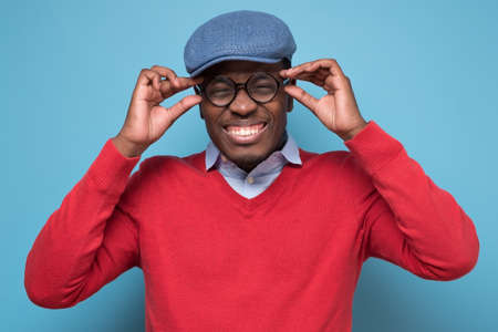 African young man wearing a pair of glasses squinting cause he can not see. Studio shot on blue wall.の写真素材