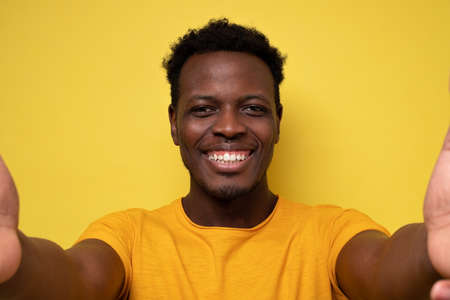 Smiling african young man making selfie on yellow background