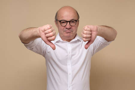 Displeased senior man in white shirt giving thumb down