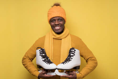 African young man in yellow hat and scarf with winter skates