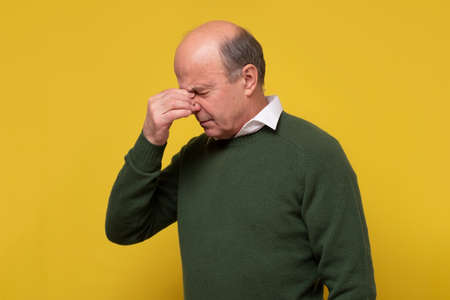 Mature man touching his nose with hand, with closed eyes, trying to concentrate