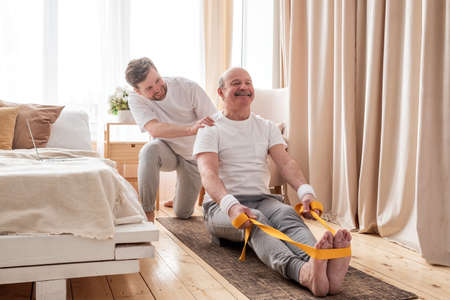 Male yoga trainer helps to senior man to do asana correctly.の写真素材