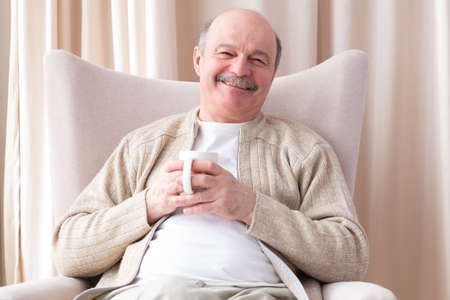 Joyful senior holding a white coffee cup and looking at the camera
