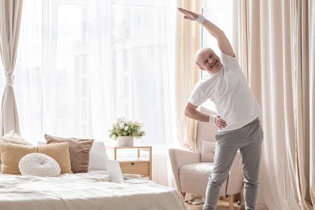 Senior bald man in yoga side stretch asana doing exercies alone at home.